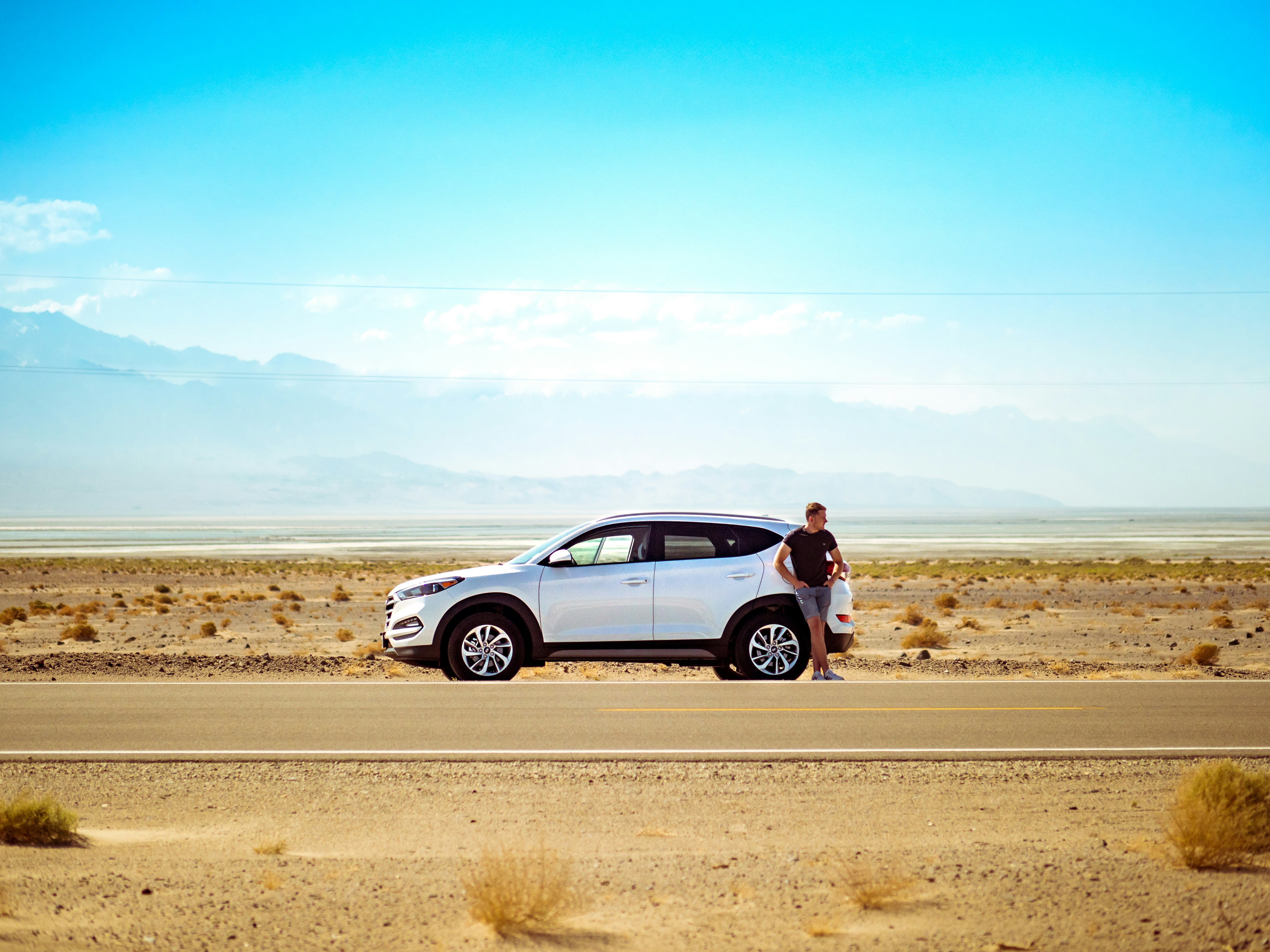 man leaning on SUV on desert road