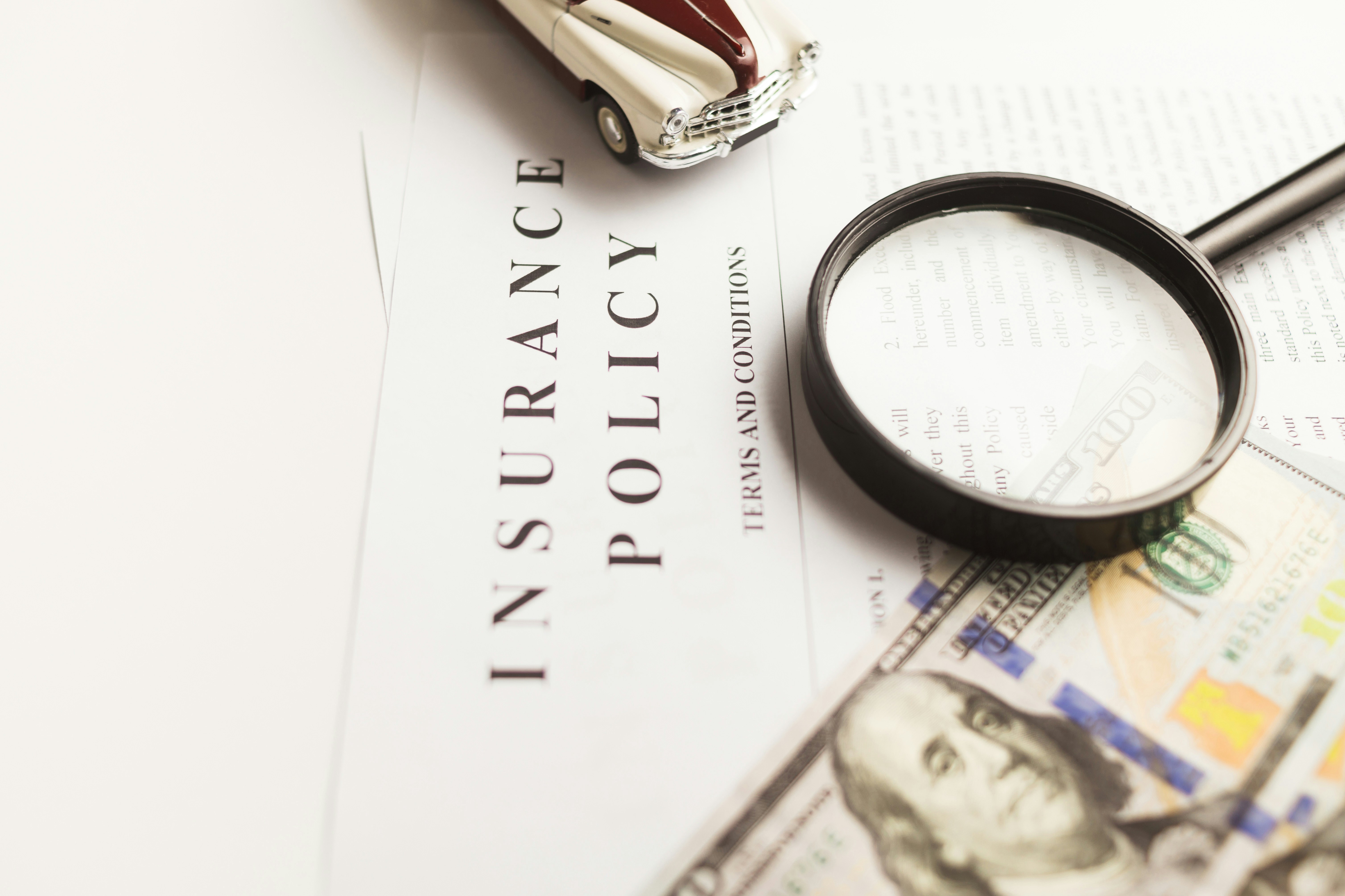 insurance policy with money, magnifying glass, and toy car