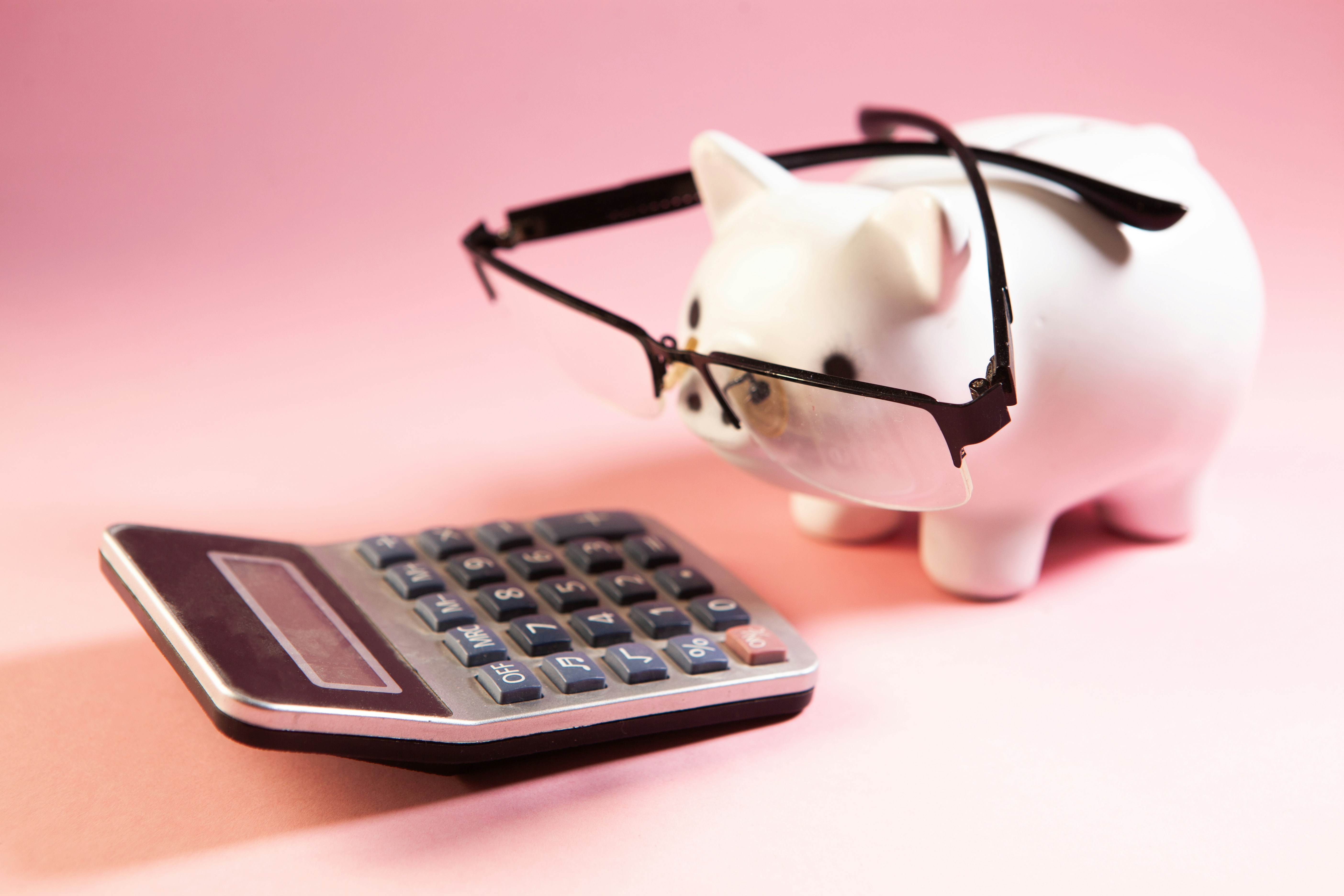 A piggy bank wearing glasses looking at a calculator