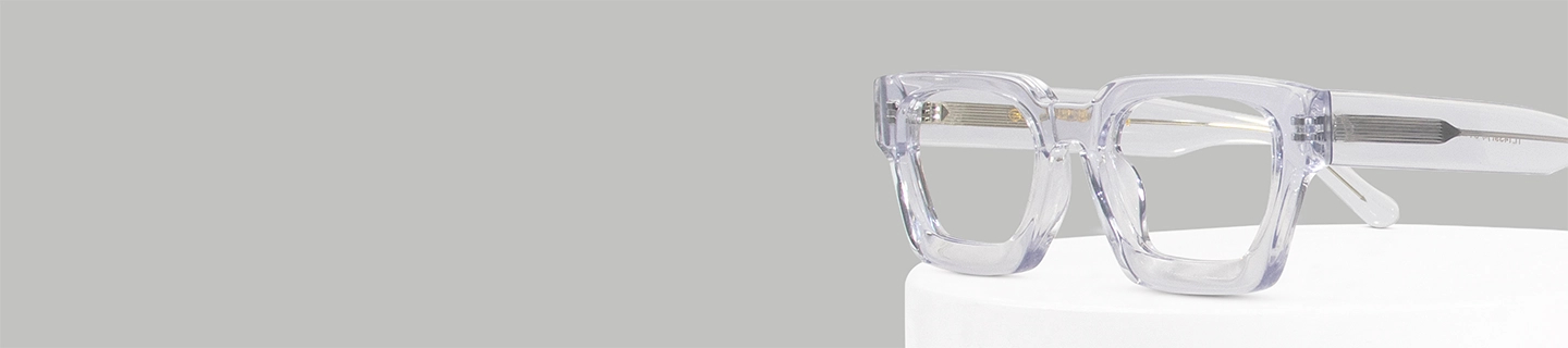 The image features a close-up of clear acetate eyeglasses in a chunky rectangular frame that is placed on a white stand against a light grey background. The image has content that says Clear Glasses. It also has a discount offer by Specscart and Trustpilot reviews.