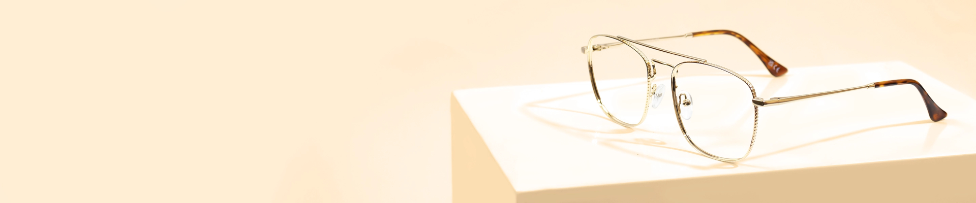 The banner features stylish glasses with gold-coloured metal rectangular frames, featuring intricate edges and tortoiseshell-patterned temple tips, presented on a white pedestal against a light beige background. The left side of the banner showcases promotional text for Gold Glasses and an Excellent Trustpilot rating.
