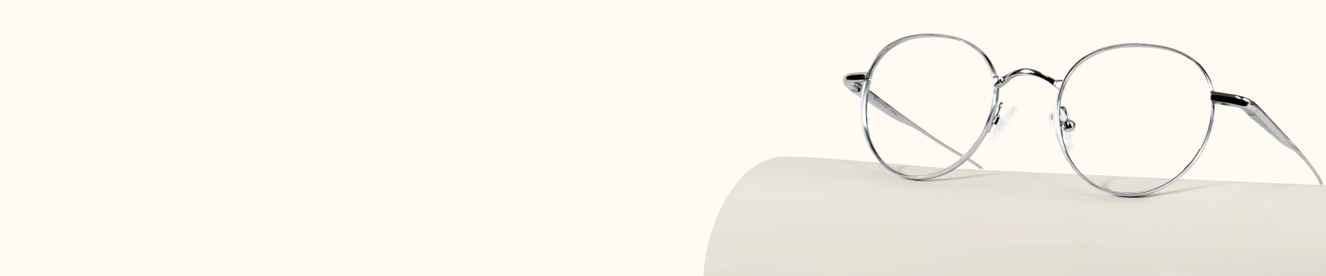 Classic round glasses with thin, minimalist gunmetal-colored metal frames resting on a light, curved surface.