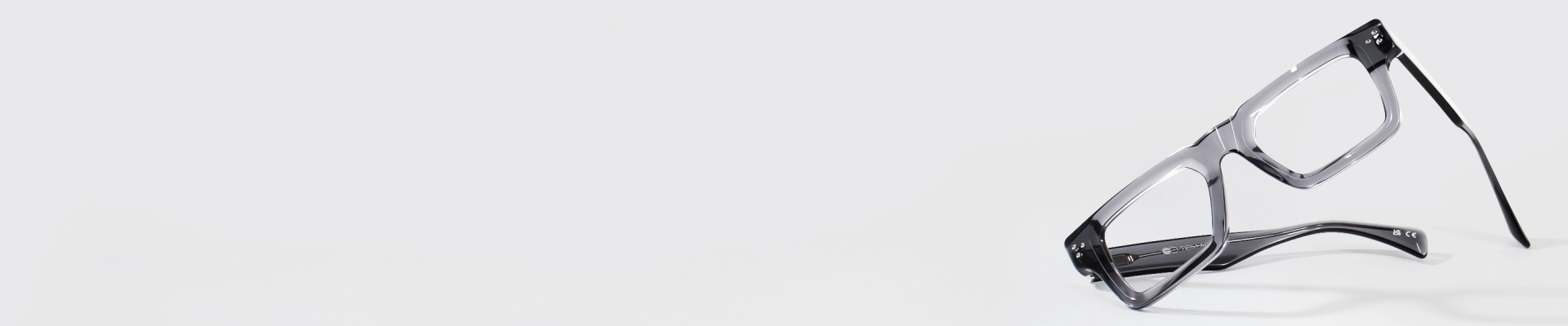 Stylish, angular square-framed glasses with glossy translucent grey frames, resting on a bright white background.
