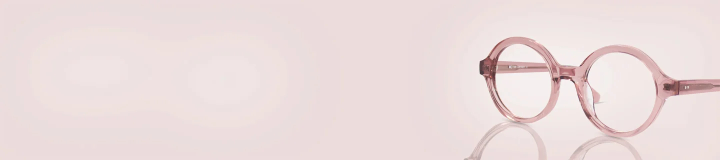 Translucent crystal pink round glasses frames resting on a reflective soft pink background, showcasing a trendy and chic monochrome aesthetic.