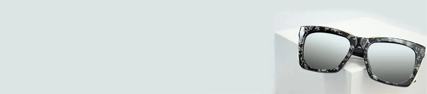 Oversized square sunglasses with silver mirrored lenses and a black and white speckled frame, resting on a white geometric block.