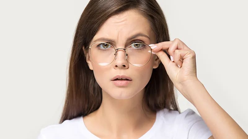 A woman adjusting her stylish round gold glasses with a puzzled expression, illustrating the common frustration of eyewear sliding down the nose.