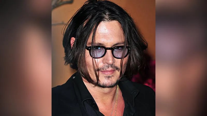 Johnny Depp with long dark hair wearing black-rimmed glasses with blue-tinted lenses and a black shirt.