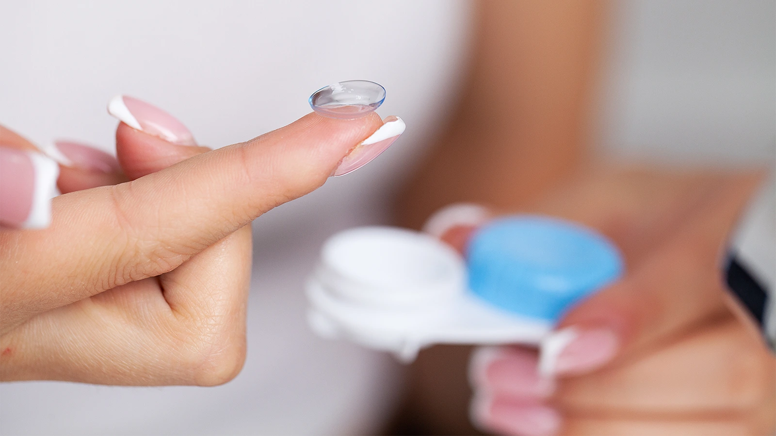 The image features a close-up of a woman's hand with a contact lens placed on the finger. A white and blue contact lens case is visible in the background.