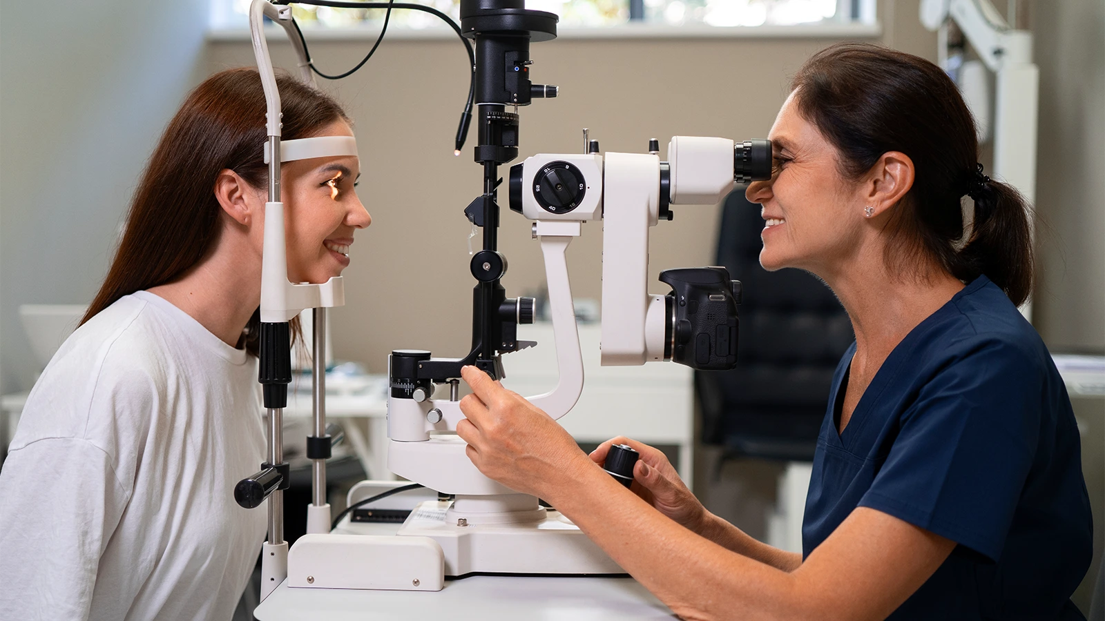 An image with an optometrist performing an eye exam on a young woman using a slit lamp biomicroscope in a clinic.