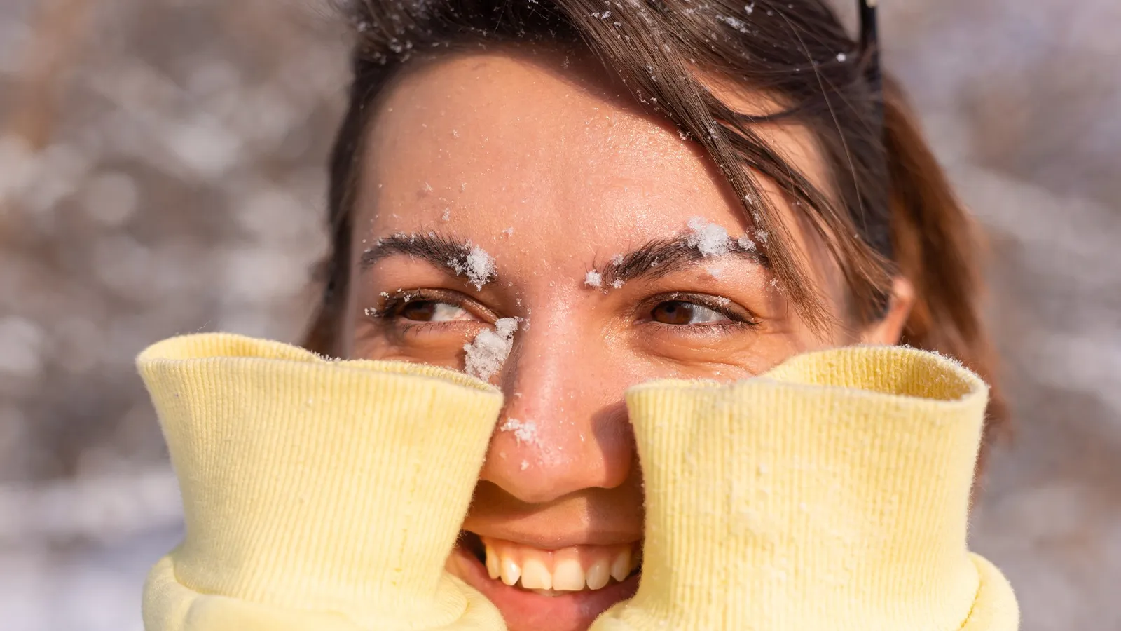 The image shows a person's eyes and face lightly covered with snow. The snow appears to have accumulated on their eyebrows, eyelashes, and the bridge of their nose, suggesting they have been exposed to a snowy or cold environment.