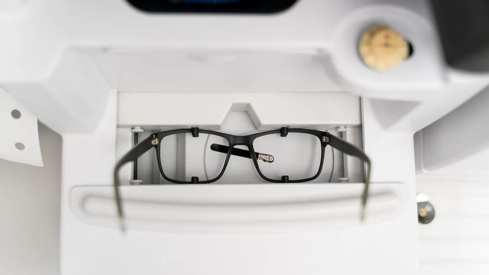 The image shows a pair of black-rimmed eyeglasses placed securely inside an optical machine. The setup suggests a process of lens cutting, adjustment, or quality testing, emphasising precision and technology in professional eyewear preparation.