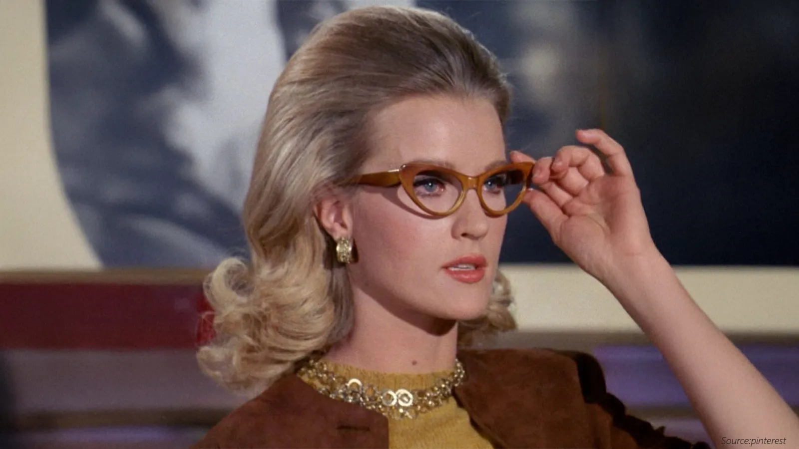 A glamorous woman in the 1960s style dons bold cat-eye glasses with golden frames, paired with voluminous blonde hair, statement earrings, and a chic necklace. The look embodies vintage sophistication and the era’s love for dramatic, stylish eyewear.