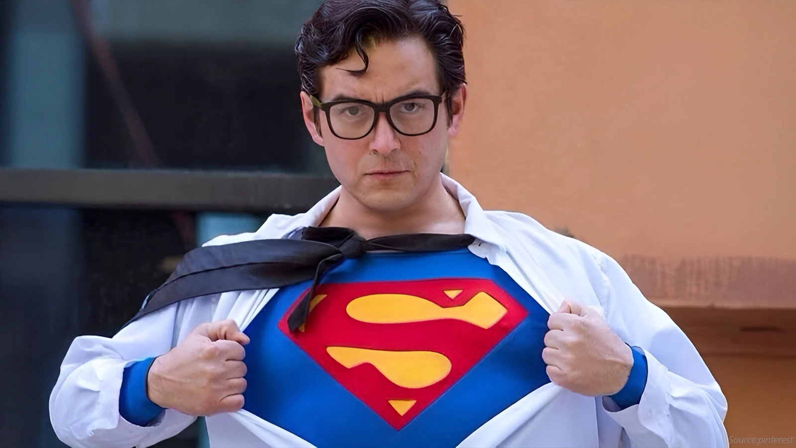 Image features Superman wearing a professional shirt, and underneath is an iconic Superman t-shirt. He also has a red tie and glasses on his face.
