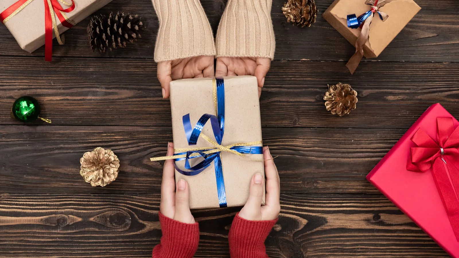 An image featuring gifting and festival season with so many gifts placed on the wooden table and hands exchanging gifts.