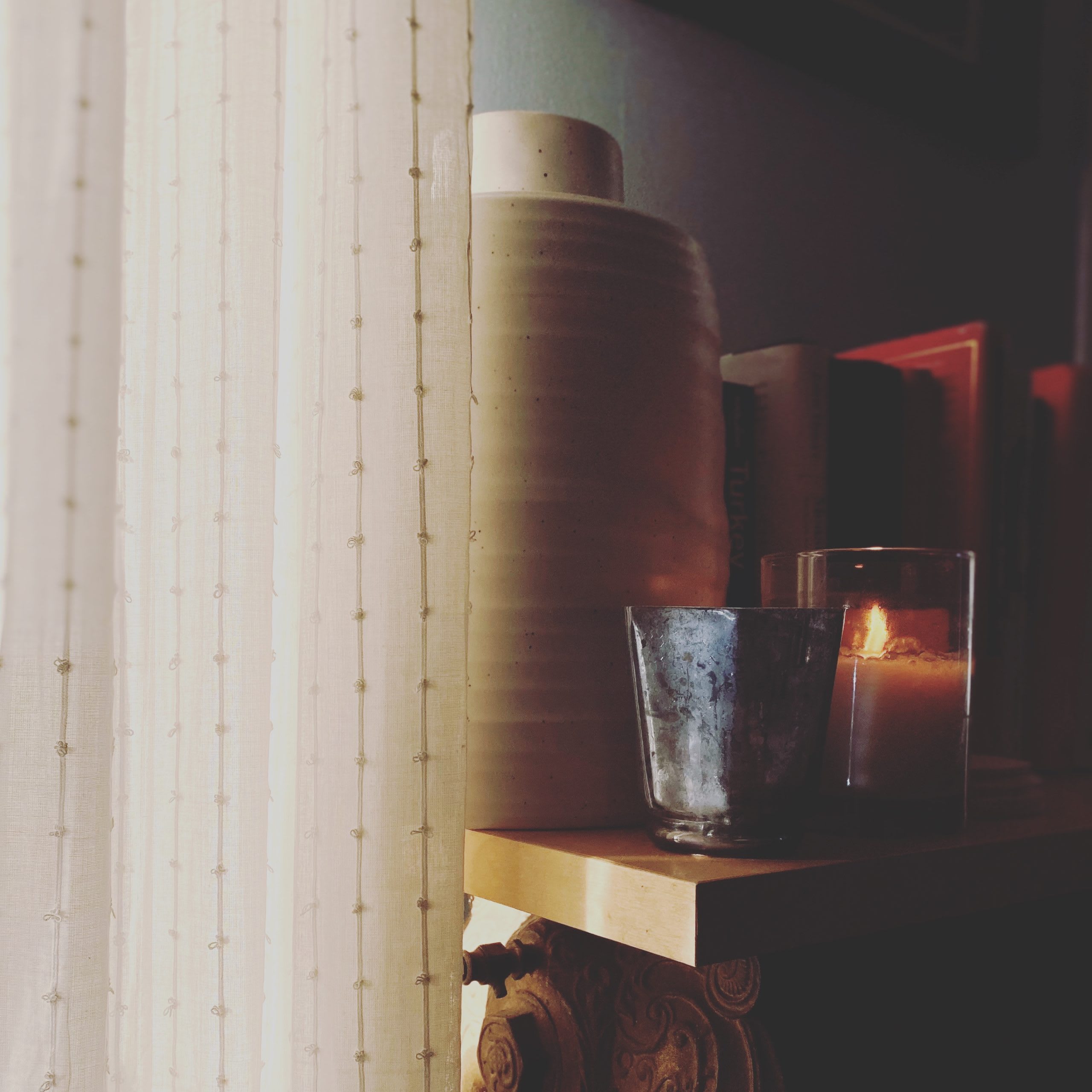 A silver cup and lit candle on a table near a textured curtain