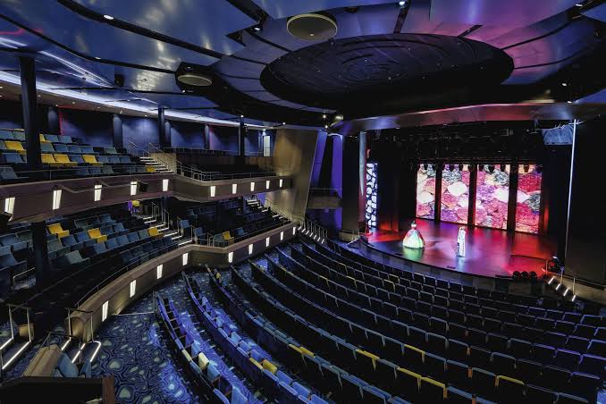 A vibrant theatre performance aboard a cruise ship with an audience enjoying the show.