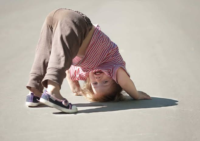 A young child bending down to look at the ground, demonstrating curiosity.