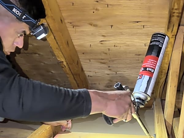 Crew member applying foam sealant in attic