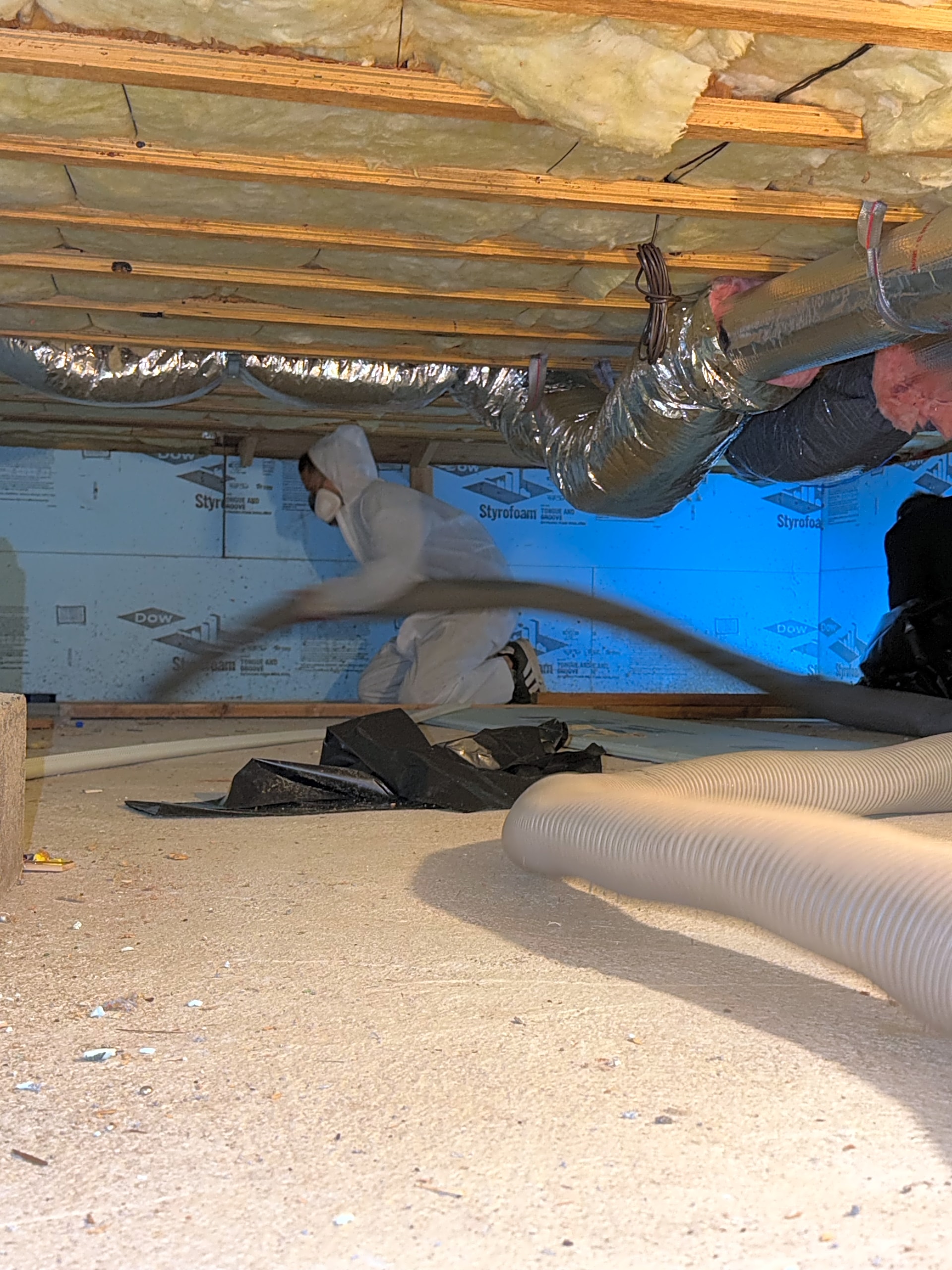 Crew working on crawl space insulation between floor joists