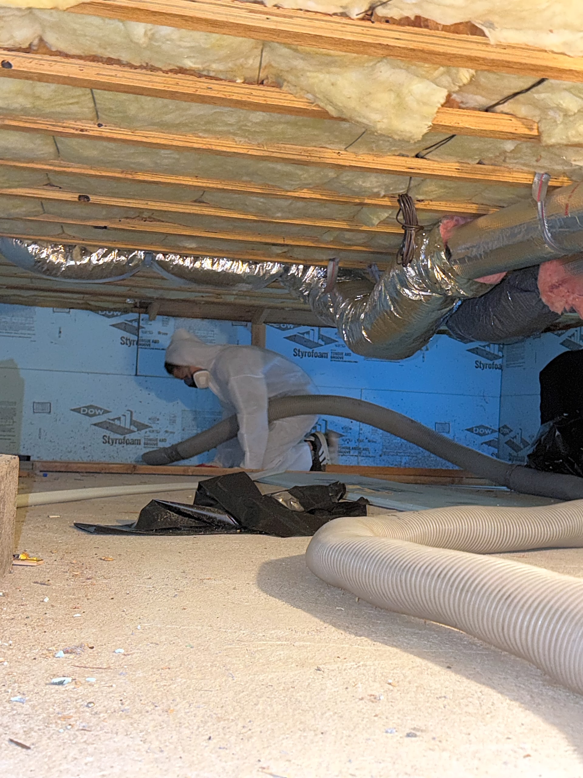 Crew inspecting and working in crawl space with insulation hoses