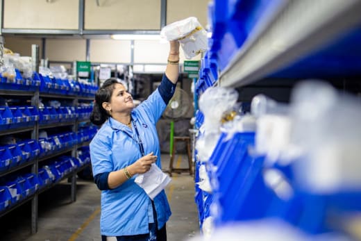Warehouse worker placing stock into blue storage bins on industrial shelving — inbound putaway and inventory