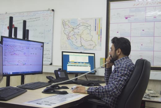 Logistics manager on the phone at a desk with multiple monitors showing schedules and operations data