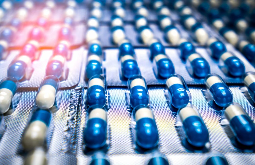 Rows of blue and white capsules packaged in blister packs; the image is brightly lit, highlighting the shiny packaging and emphasizing the uniform arrangement of the medication.