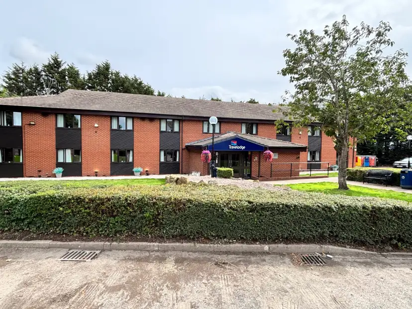 Travelodge Hartlebury exterior viewed from the car park forecourt, showing the set-back roadside hotel with tidy gardens and level access entrance