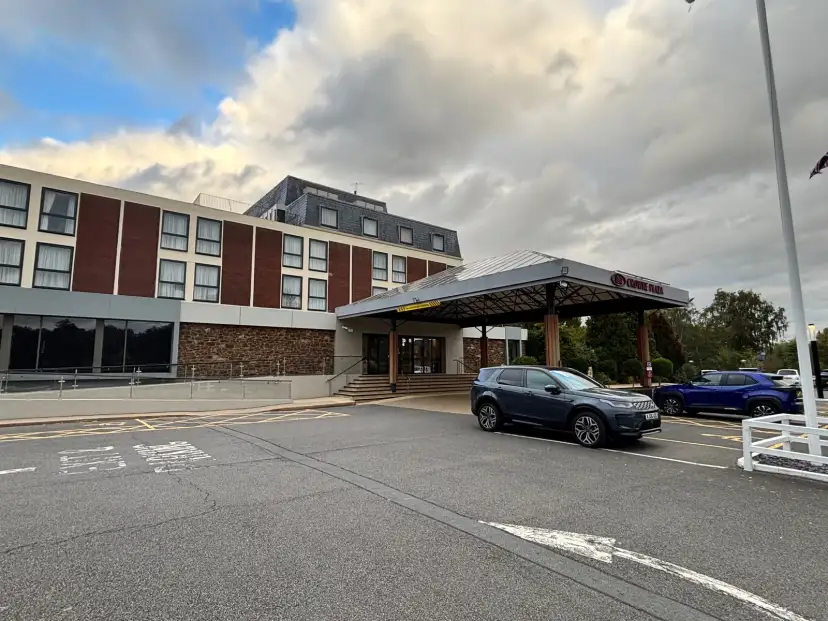 Crowne Plaza Stratford Upon Avon hotel entrance with automatic sliding doors, riverside setting visible behind, mature trees in background
