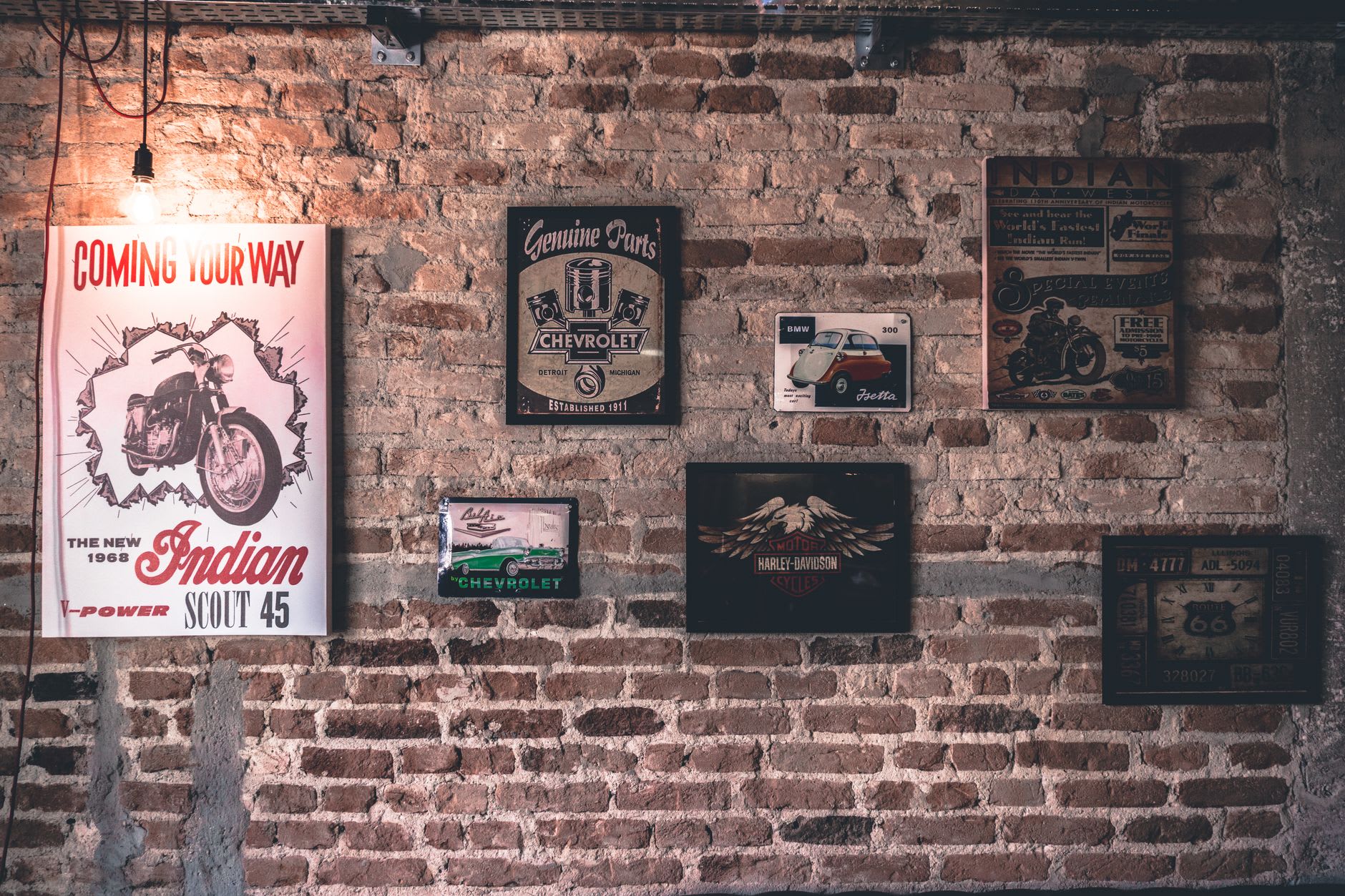 Vintage automotive tin signs and motorcycle posters mounted on a rustic exposed brick garage wall