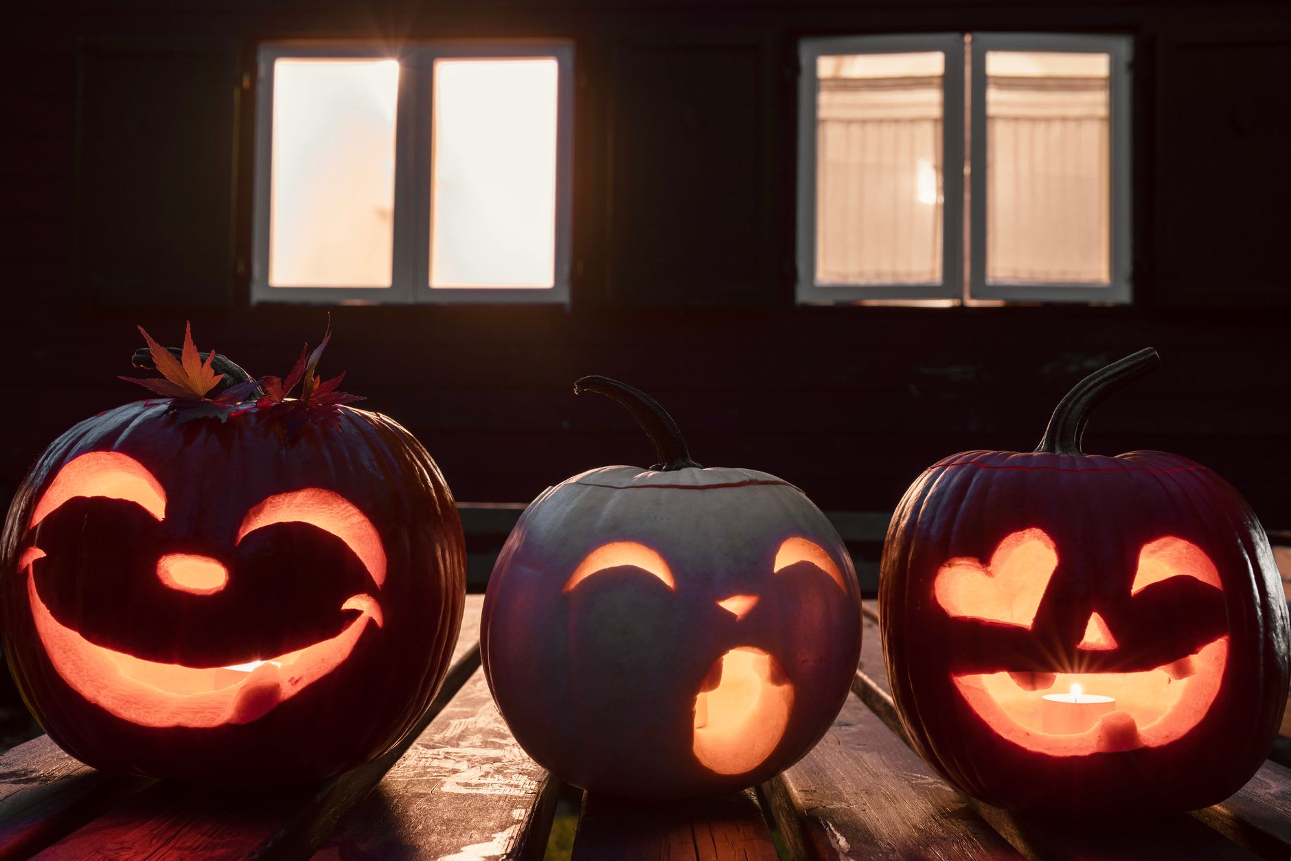 Three smiling carved jack-o'-lantern pumpkins glowing with candles on a wooden deck at dusk.
