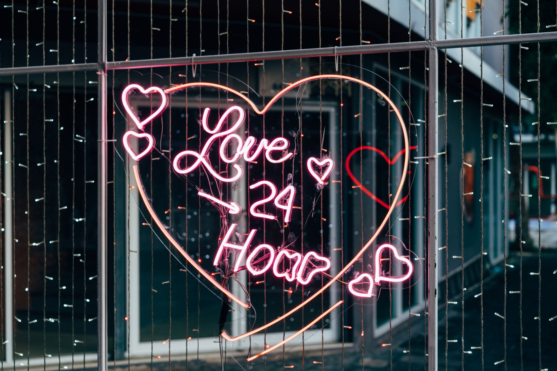 Pink heart-shaped neon sign reading '24 Hour' glowing on a city street