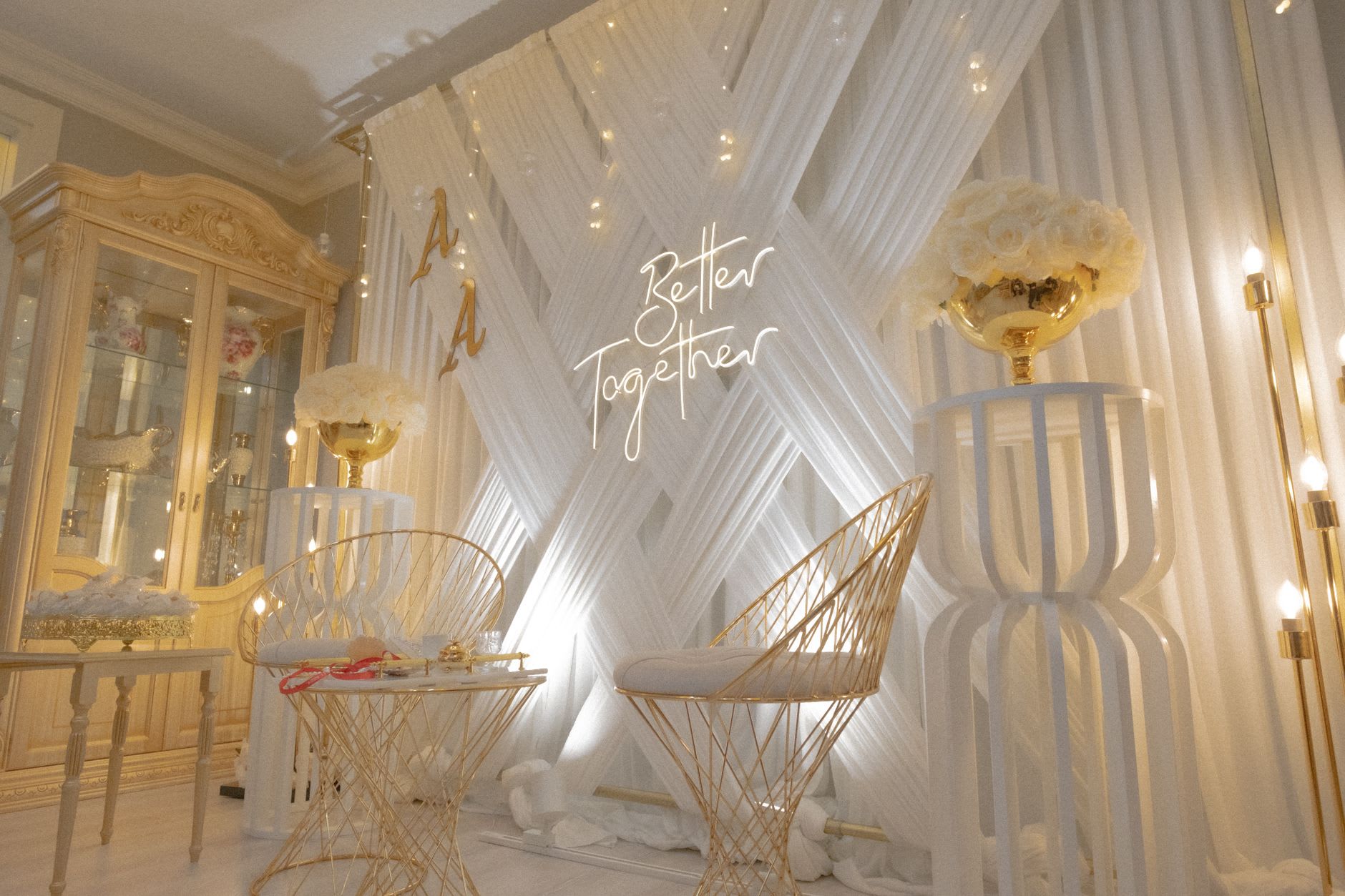 A cursive 'Better Together' neon sign on a white draped backdrop in an elegant gold-accented event setting.