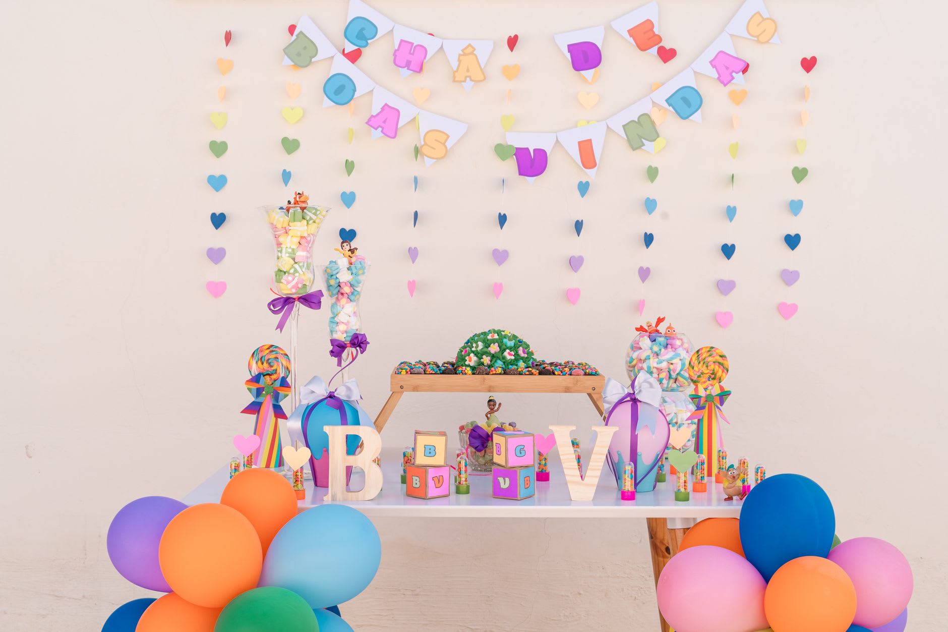 Colorful baby shower dessert table with a balloon arch, heart garlands, candy jars and pastel bunting