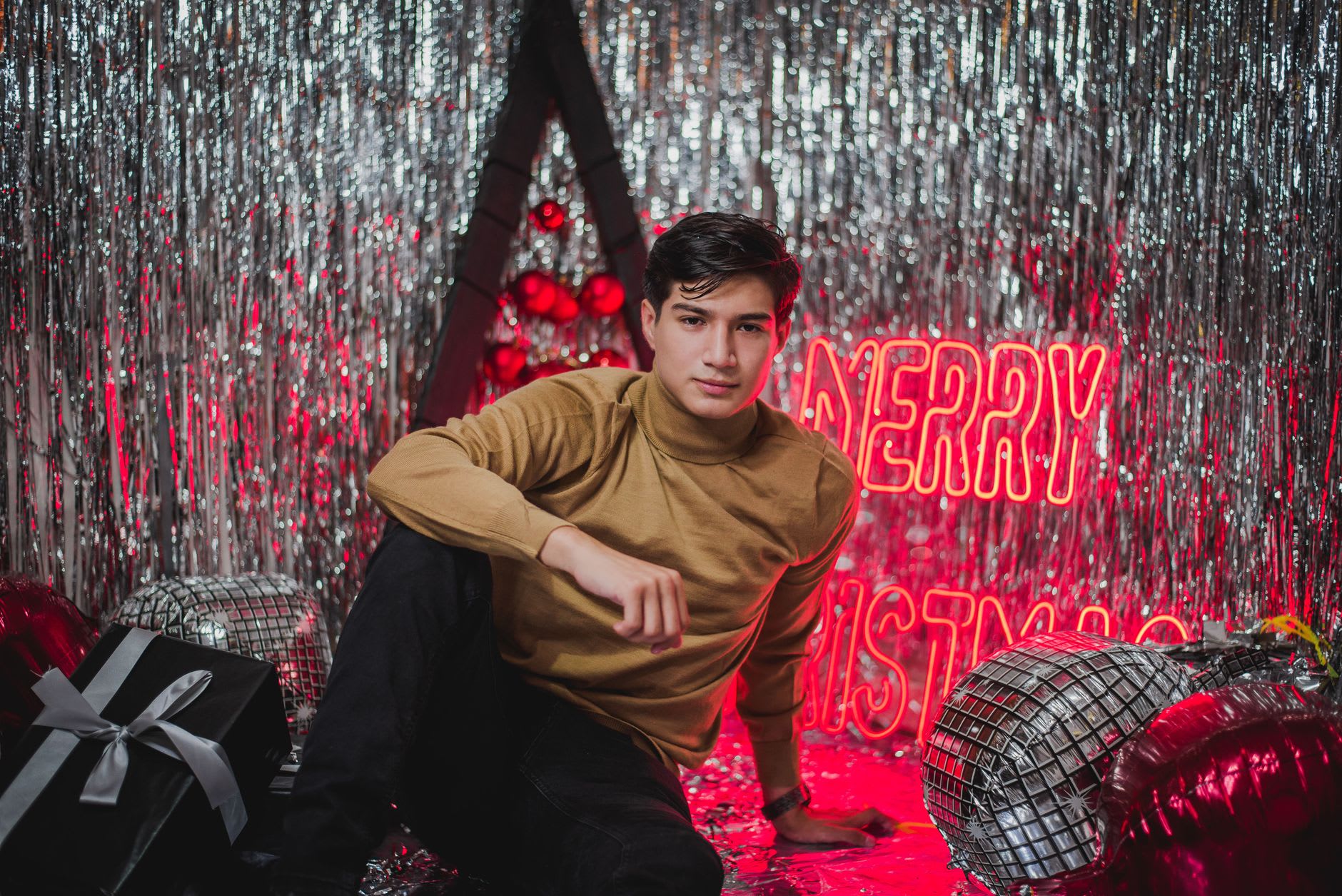 Young man posing in a festive setting with holiday decorations and warm neon lighting
