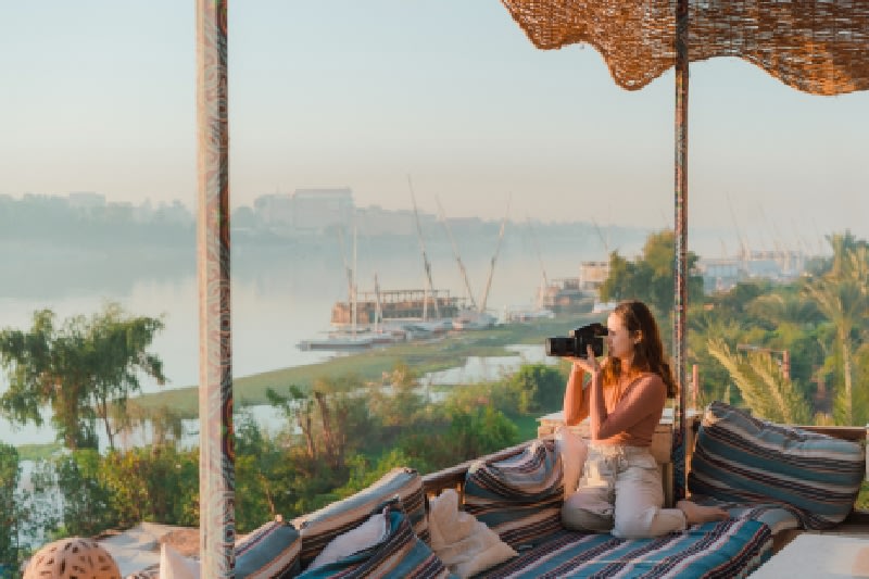 Joven sentada en la terraza y fotógrafa Nile al atardecer en Luxor