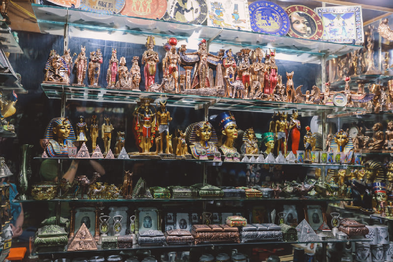 Figuras y recuerdos del antiguo Egipto en una vitrina: estatuas de faraones, Nefertiti, pirámides y amuletos tradicionales.