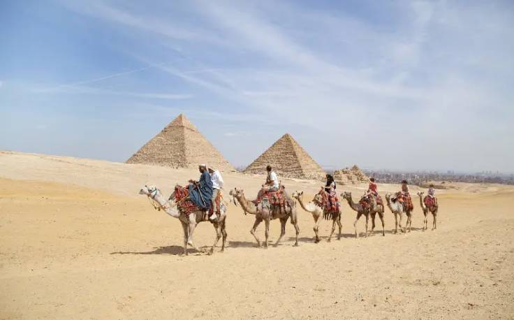 un gruppo di turisti cavalcano cammelli davanti alle piramidi di giza