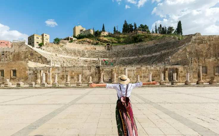 ragazza con cappello in piedi a braccia aperte davanti al teatro romano, viaggio in giordania cosa mettere in valigia
