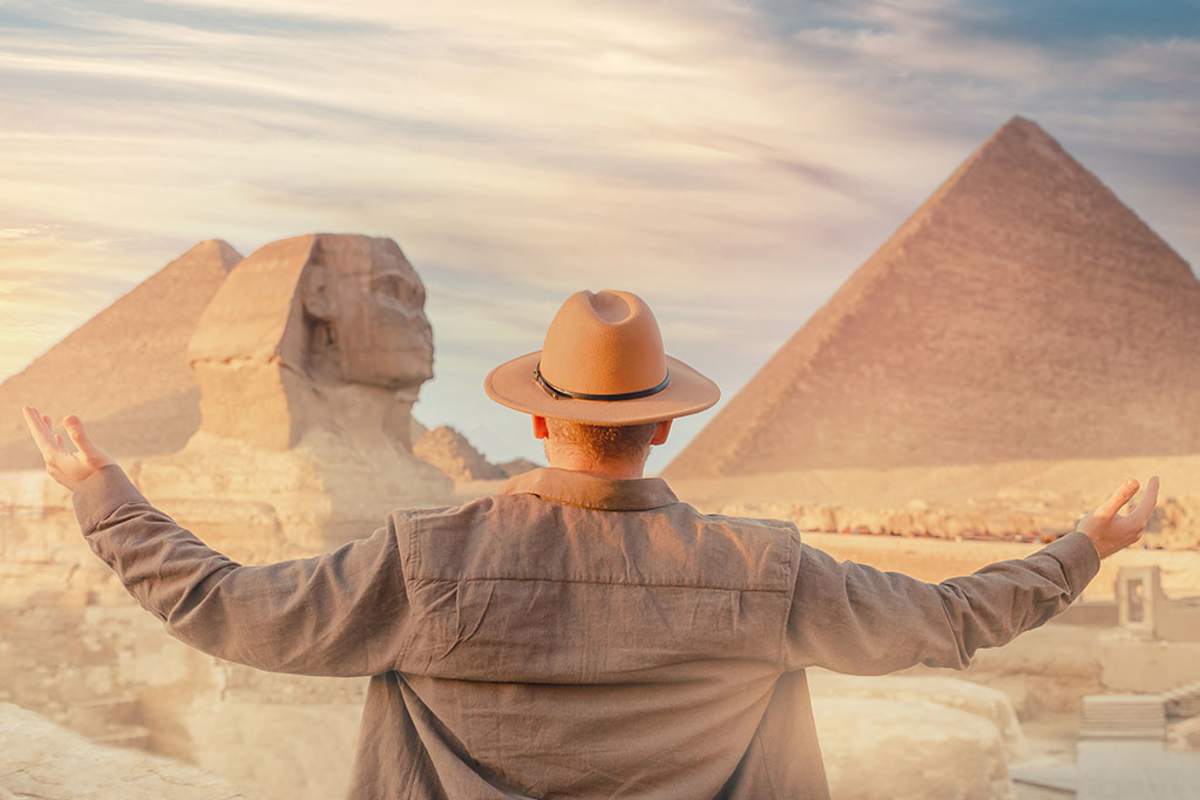 a happy traveller with a hat infront of pyramids if Giza
