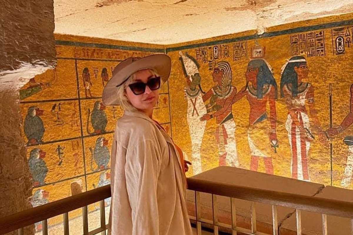 Tourist in wide-brimmed hat standing before vibrant hieroglyphic wall inside an ancient Egyptian tomb.