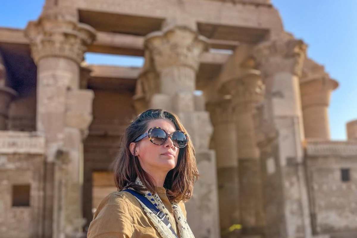 Visitor in sunglasses standing before the carved stone columns of the Temple of Kom Ombo under bright sunlight