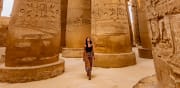 a girl in black shirt and printed pants walking happily in an incient egyptian temple 