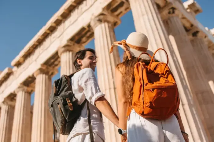 a tourist couple holding their hands in front of the Parthenon temple
