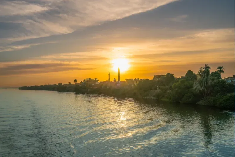 Goldener Sonnenuntergang über dem Nil bei der Schleuse von Esna mit Minarett und Palmen