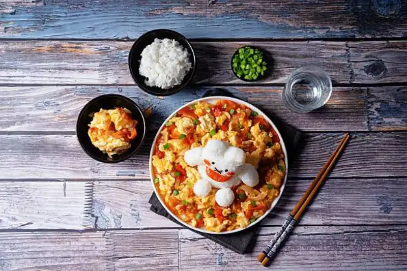 Asiatische Tomaten-Eier serviert mit Reis, der kunstvoll in Form eines Hasen auf einem weißen Teller arrangiert ist.