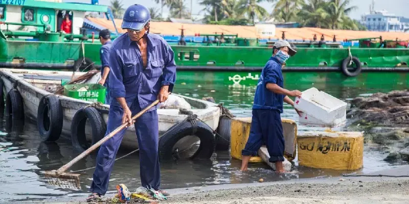 Trabajadores locales limpiando y recogiendo basura en la orilla de la playa de la isla de Phu Quoc.