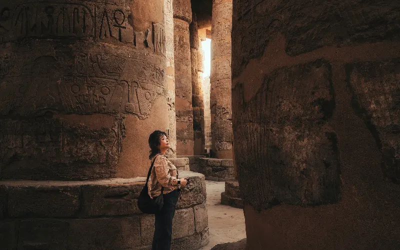 Chinese woman traveler admiring the towering hieroglyphic columns of Karnak Temple in Luxor, Egypt