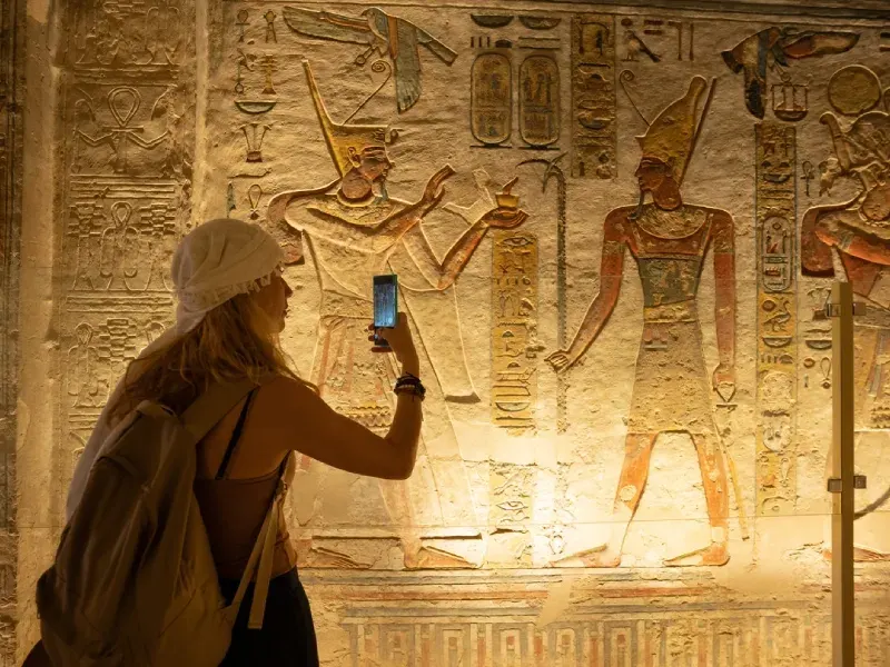 Una donna usa il suo smartphone e scatta foto mentre visita le stanze interne della tomba di Ramses IX, KV6, nella Valle dei Re, a Luxor, in Egitto.