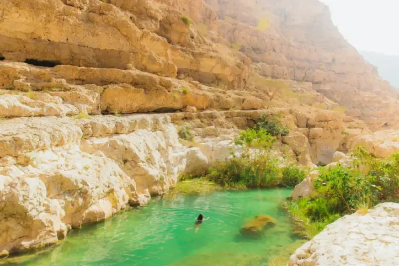 Vista dall'alto di una donna che nuota nelle acque verdi del canyon di Wadi Ash Shab, tra i paesaggi desertici dell'Oman.